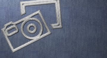 Silver Stitched Camera Logo on Blue Material